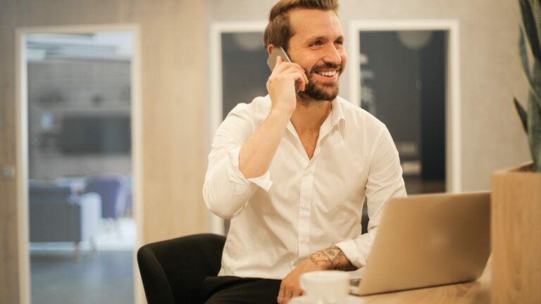Smiling man sitting at office desk talking on mobile phone