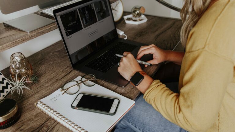 woman working on laptop with notebook and phone in foreground