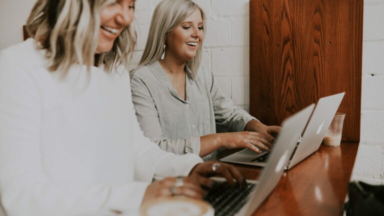 Two women smiling whilst working on laptops
