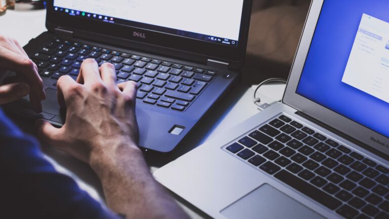 close up of hands working on laptop with another laptop beside him