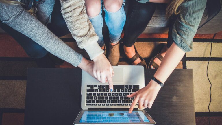 3 people all pointing at laptop screen, viewed from above