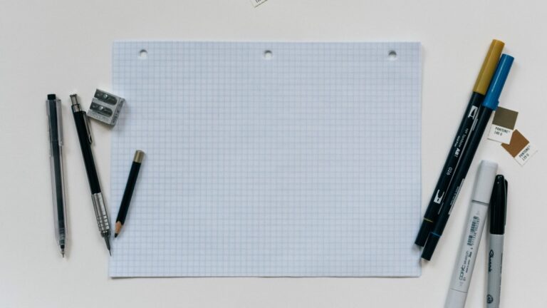 squared paper on desk with pens and pencils, viewed from above