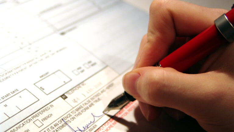 Close up of a hand holding a pen, signing their name on a form