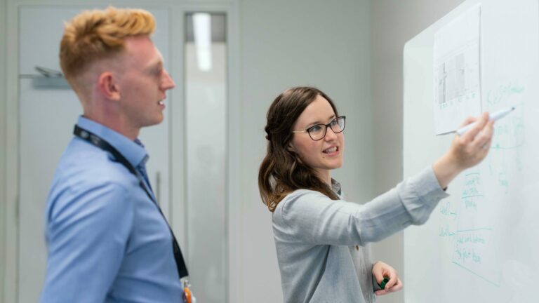 woman writing on white board while man observes