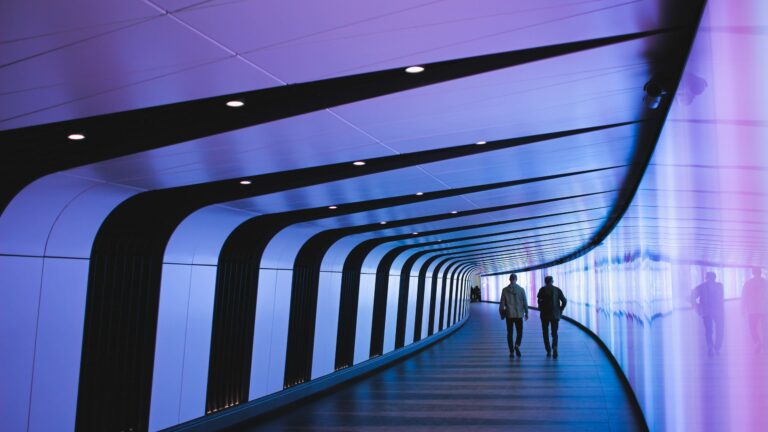 2 people walking along neon purple illuminated corridor