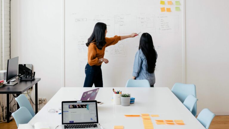 two women in an office standing at whiteboard with diagrams and post-it notes