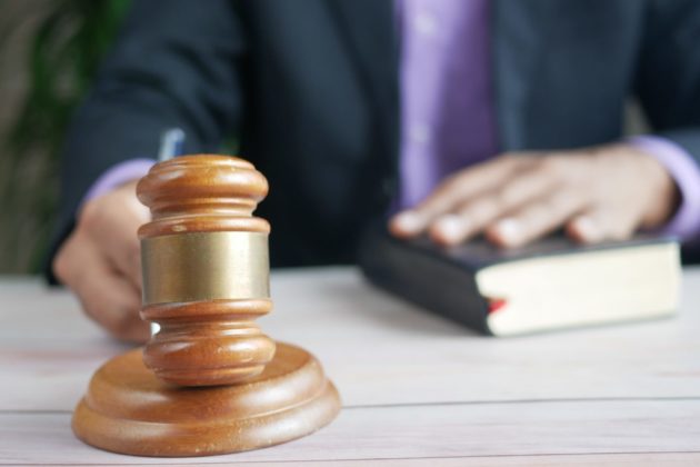 close up of a hand using a hammer and gavel with the other hand resting on a book