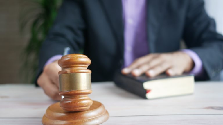 close up of a hand using a hammer and gavel with the other hand resting on a book