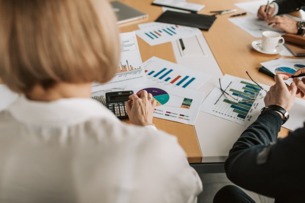 Woman seen from behind using a calculator on desk covered with diagrams of graphs.